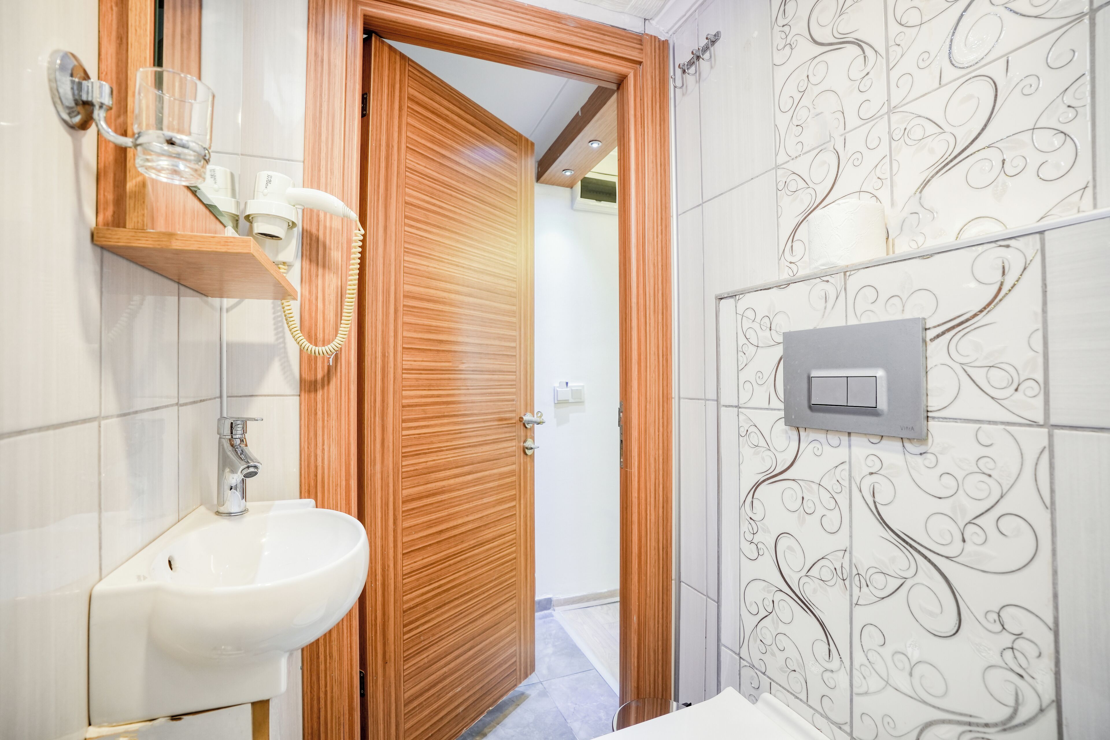 A bathroom with a wooden door, a white sink, and a wall-mounted light switch.