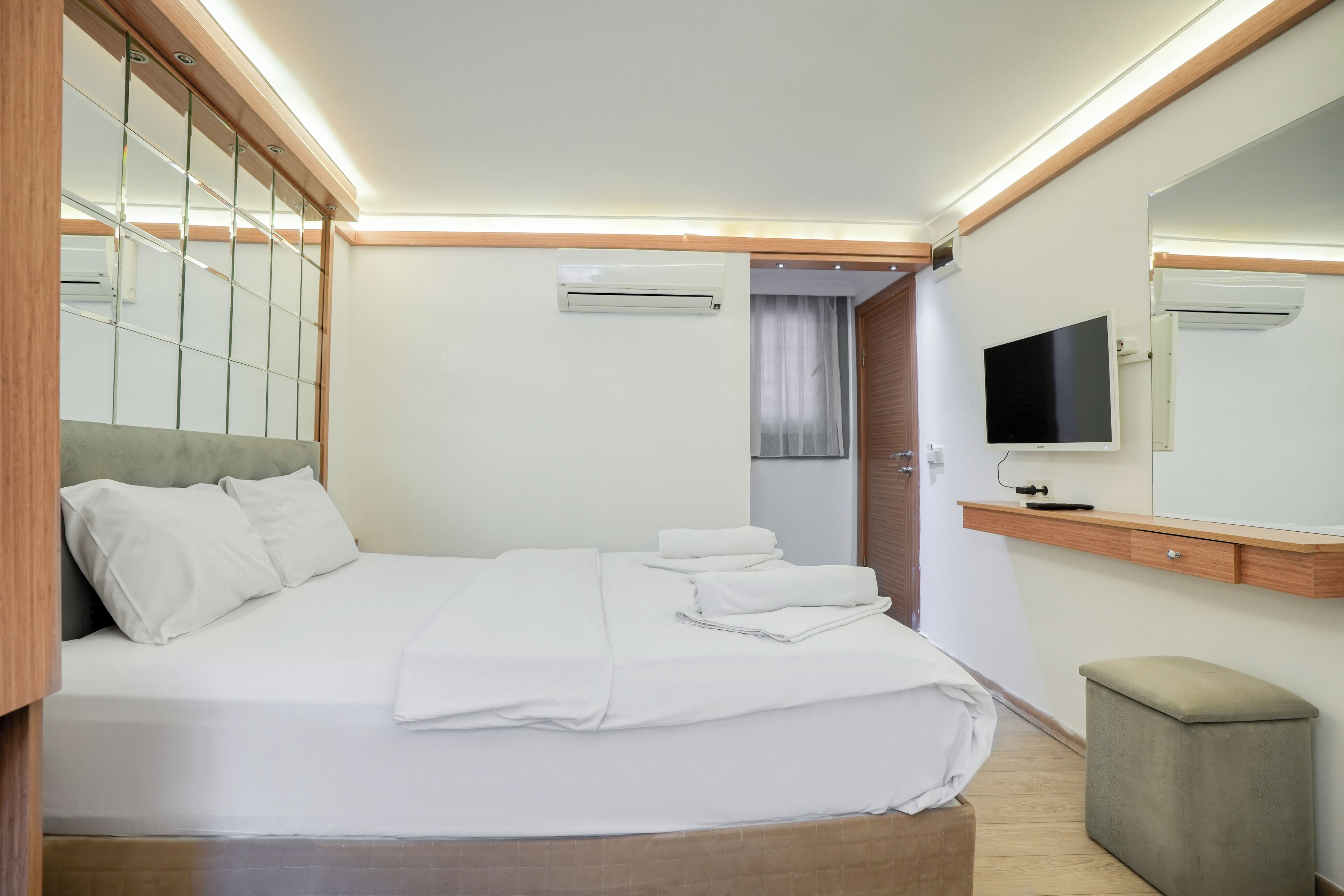 A neatly made bed with white linens, a wooden headboard, and a bedside table with a flat-screen TV.