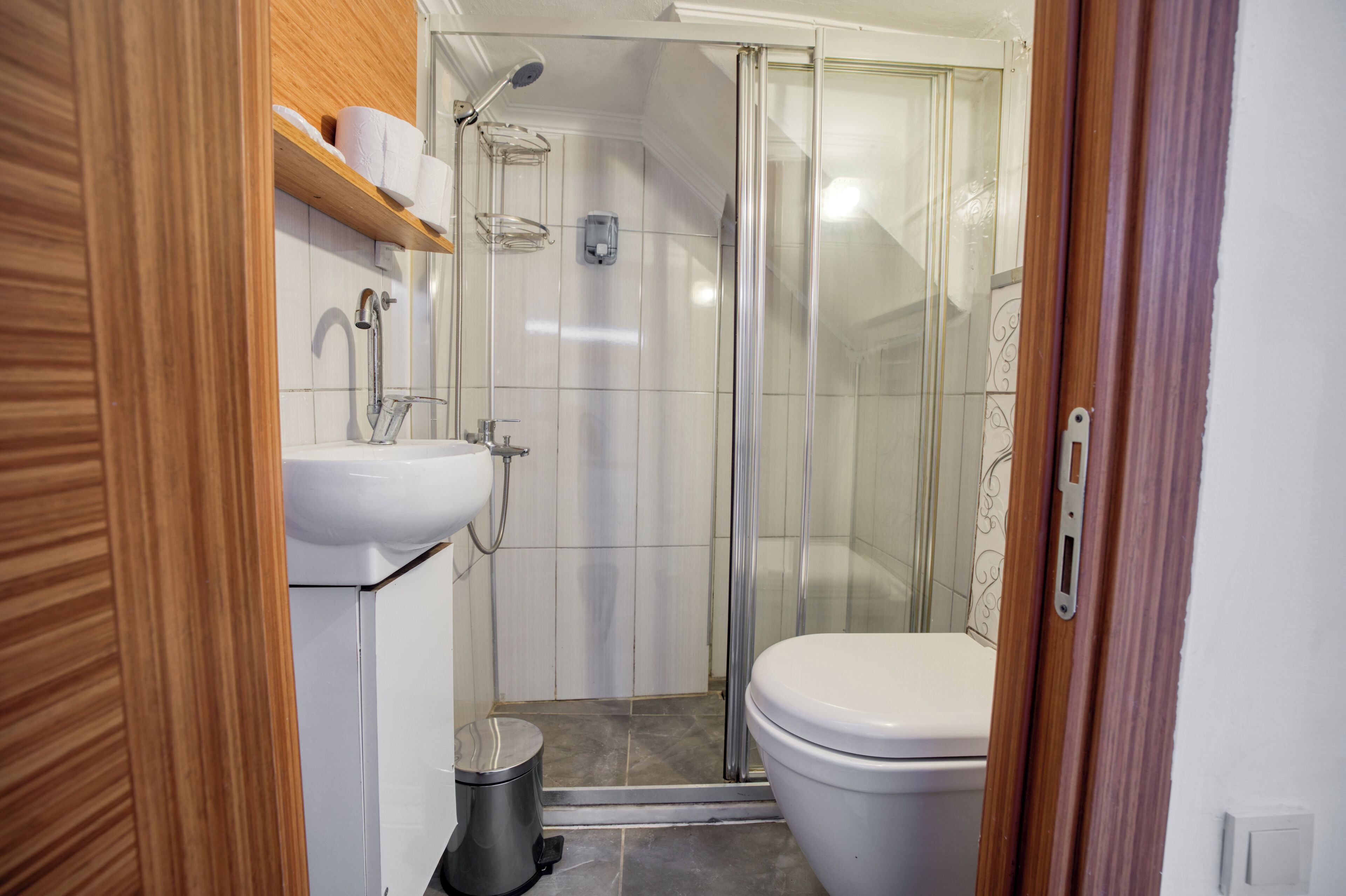 Baño con ducha, inodoro, lavabo y estantes de madera.