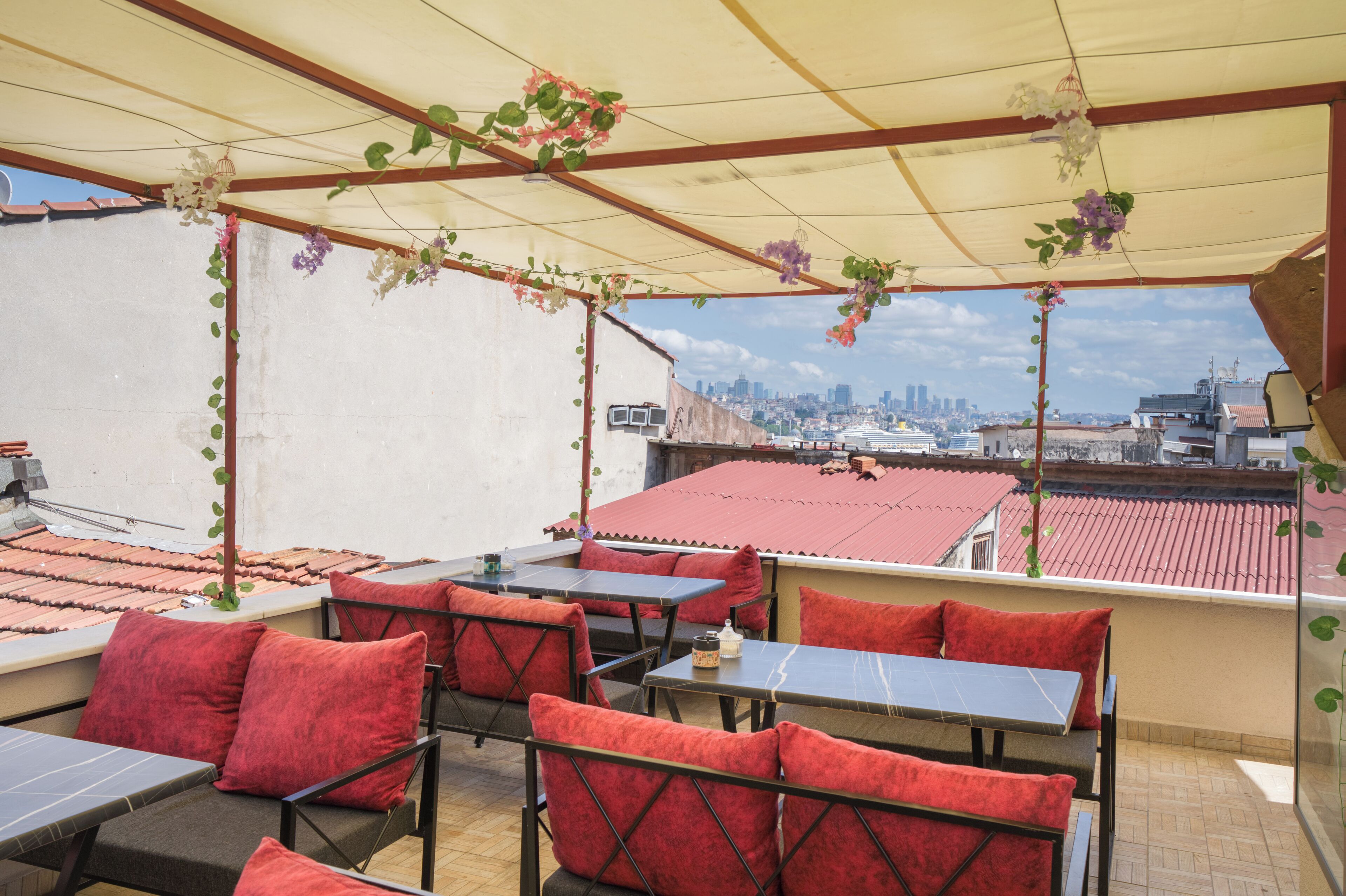 An outdoor terrace with red cushioned seating, a table with a bottle, and hanging plants.