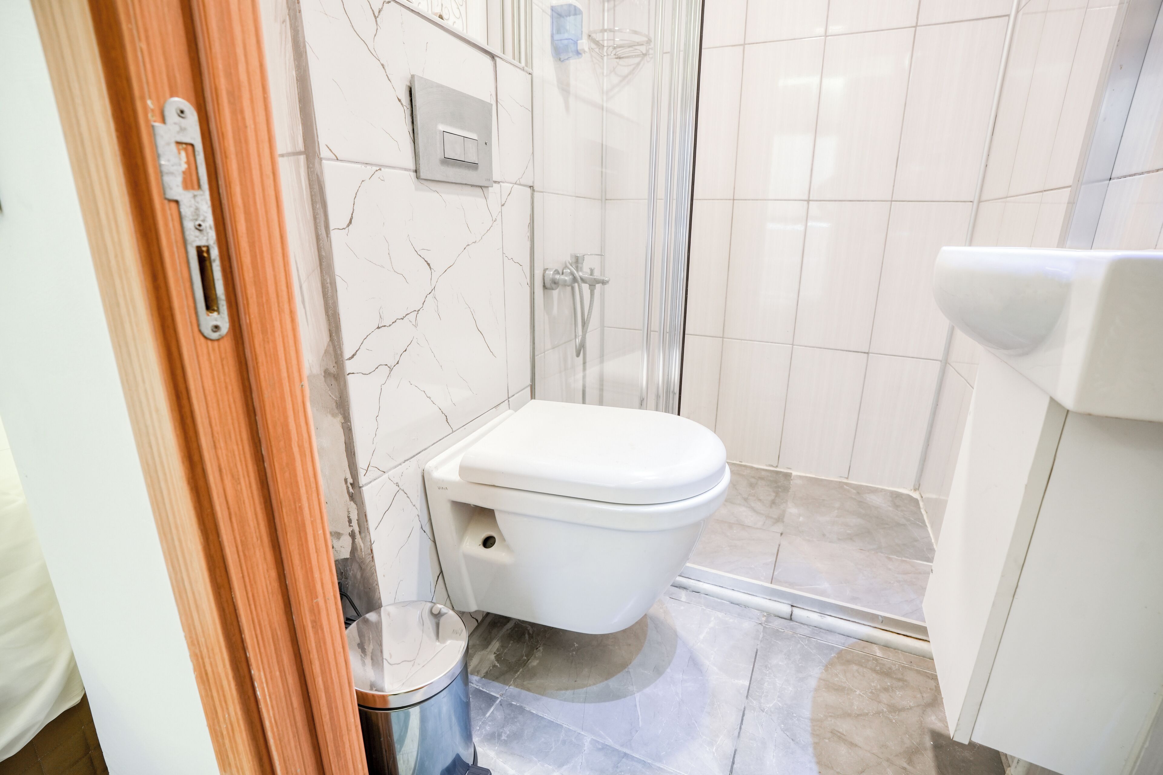 A bathroom with a white toilet, a glass shower enclosure, and a marble floor.