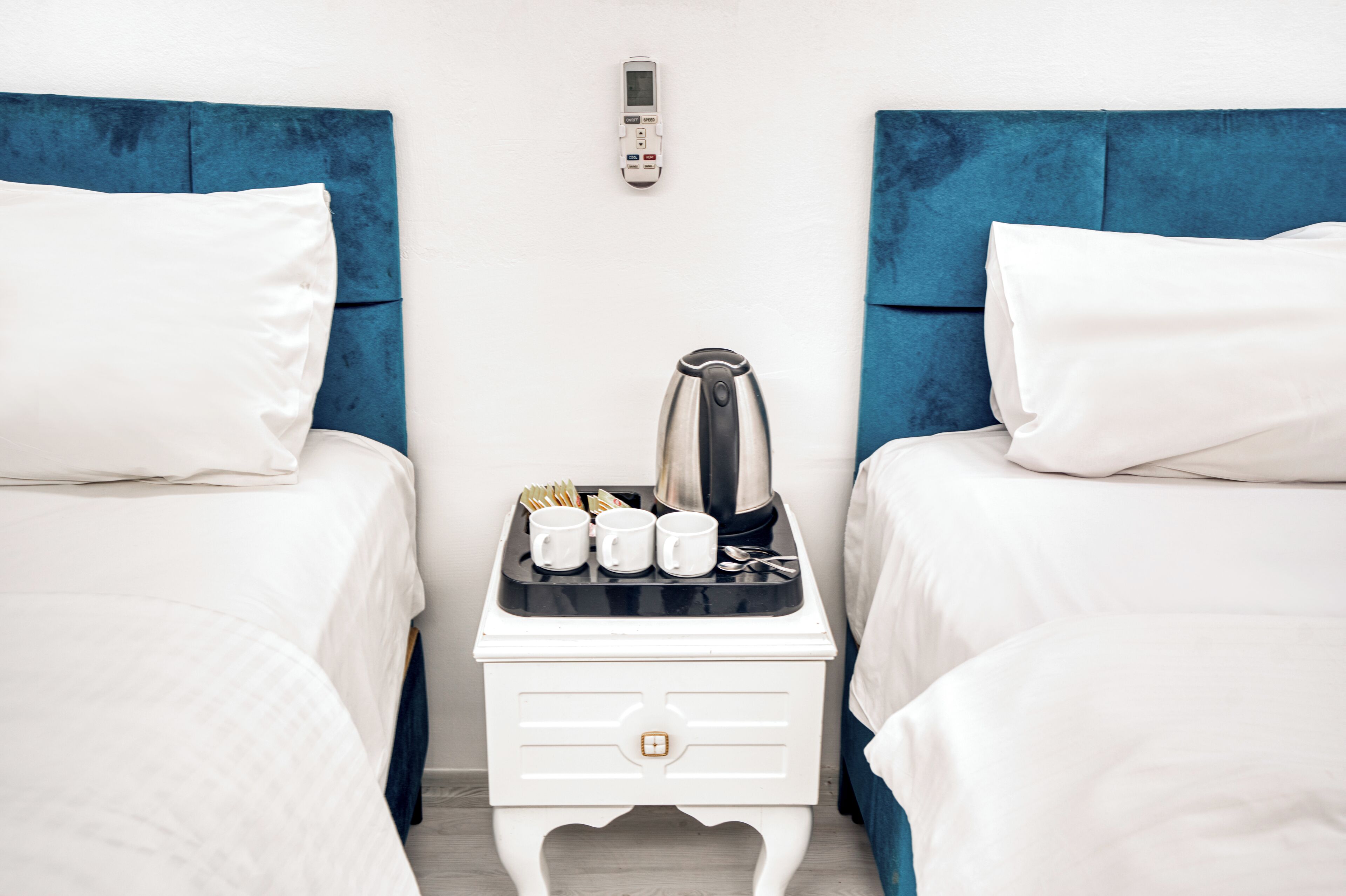 Une chambre d’hôtel avec deux lits, une table de chevet avec une bouilloire, des tasses et une télécommande.