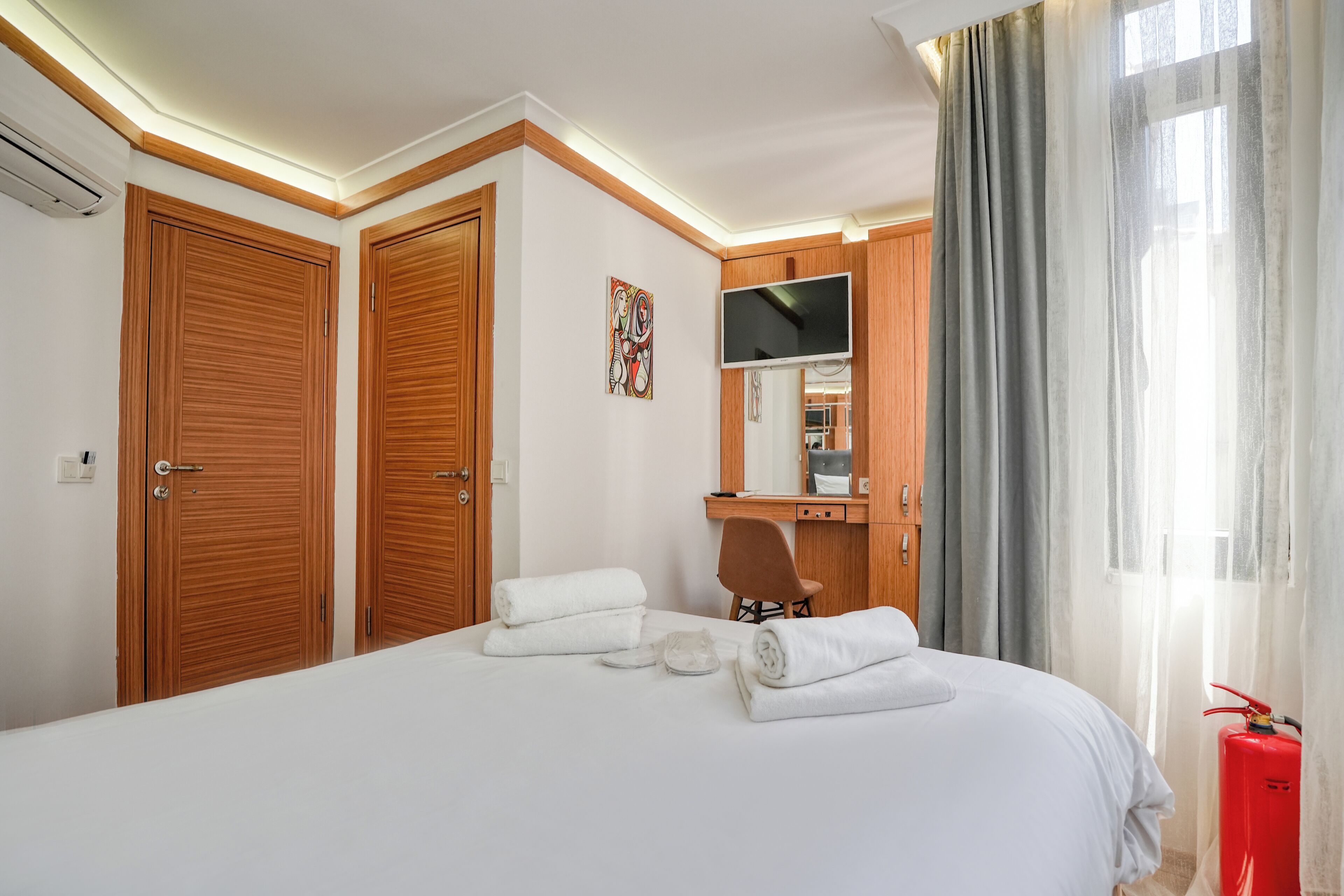 Ein Hotelzimmer mit einem großen Bett, einem Holzschrank, einem Schreibtisch mit Stuhl, einem Fernseher und einem Feuerlöscher.