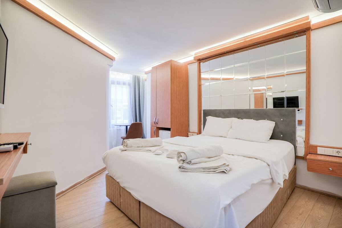 Una moderna camera d'albergo con un letto grande, una testiera in legno e uno specchio ampio.