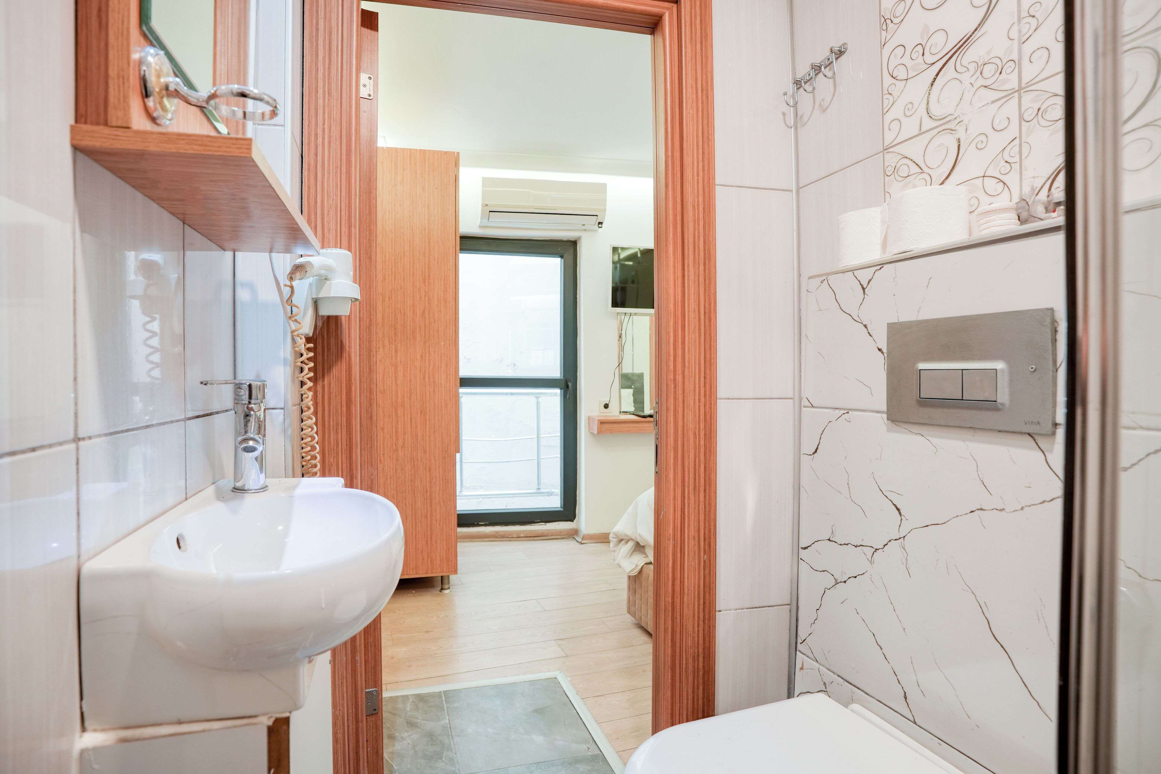 A modern bathroom with a white sink, wooden vanity, and a marble backsplash.