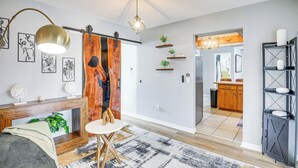 A modern living room with a wooden console table, a round white table, and a hanging light fixture. - 6 Mi to Gemini Springs Park: Chic Home w/ Pool! (Deltona)