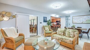 A living room with wicker furniture, a glass coffee table, and a dining area with a wooden table and chairs. - 6 Mi to Gemini Springs Park: Chic Home w/ Pool! (Deltona)