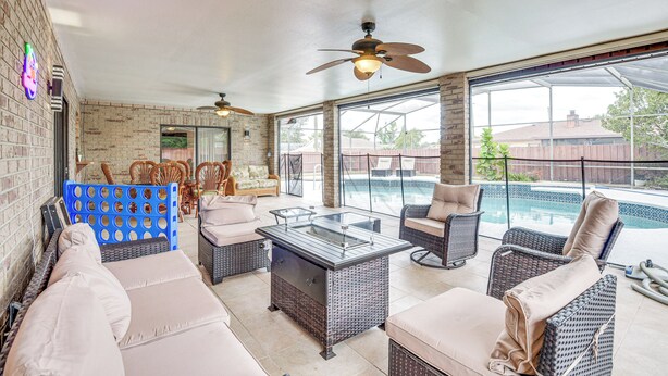 A covered patio area with wicker furniture, a glass-top table, and a ceiling fan. - 6 Mi to Gemini Springs Park: Chic Home w/ Pool! (Deltona)