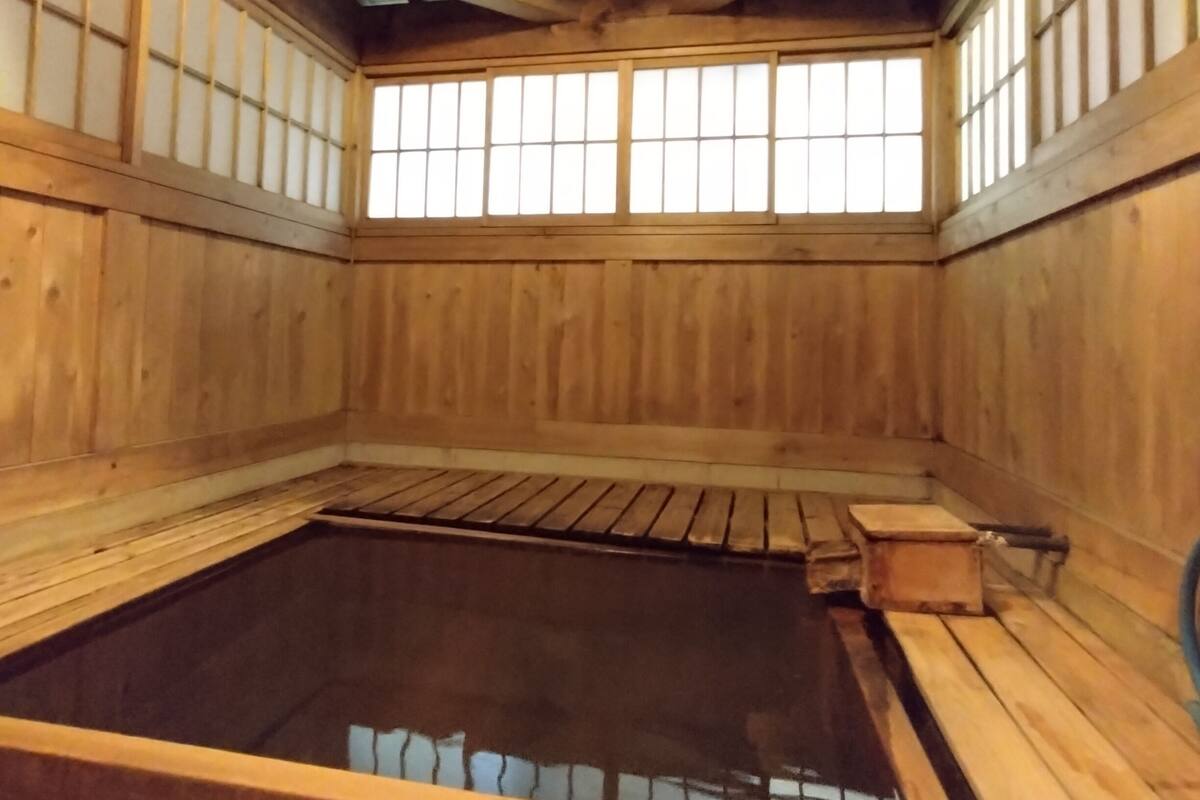 Un balneario tradicional de madera con una fuente termal central, vigas de madera y puertas correderas shoji.