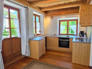 Une cuisine compacte avec des meubles en bois, un four encastré et une fenêtre donnant sur un paysage verdoyant.