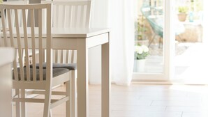 Een eethoek met een witte tafel en stoelen, een lamp en uitzicht op een tuin door een glazen deur.