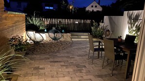 Een terras buiten met tegels, rieten meubels en potplanten.