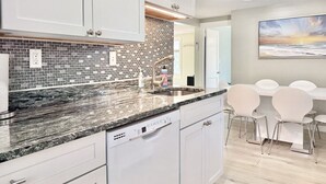 Une cuisine moderne avec des armoires blanches, un comptoir en granit et un pare-feu en petites carreaux. On y trouve également un coin repas avec une table et des chaises.