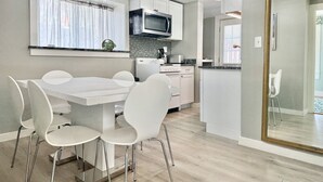 Une cuisine moderne avec des meubles blancs, un four à micro-ondes et un coin repas comprenant une table et des chaises blanches.