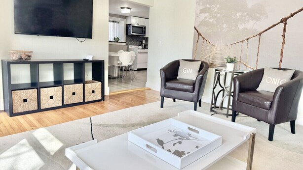Un salon moderne doté d’un téléviseur à écran plat, de deux fauteuils en cuir, d’une table basse blanche et d’un meuble de rangement noir avec des paniers.