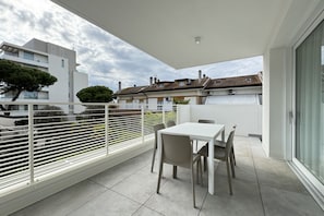 A balcony with a white table and chairs, a view of neighboring buildings, and a white railing.