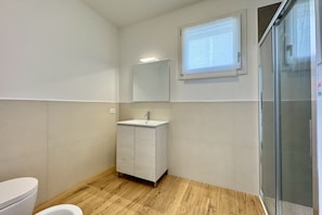 A bathroom with a toilet, a sink, a mirror, and a shower.