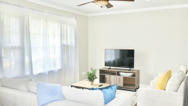 A living room with a sofa, a coffee table, a TV, and a ceiling fan. - Spacious Stay Near Carowinds Amusement Park | Newly Remodeled | Fenced Yard | Pet & Family Friendly (Pineville)