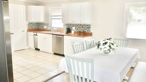 A kitchen with white cabinets, a tiled backsplash, and a dining table with chairs. - Spacious Stay Near Carowinds Amusement Park | Newly Remodeled | Fenced Yard | Pet & Family Friendly (Pineville)