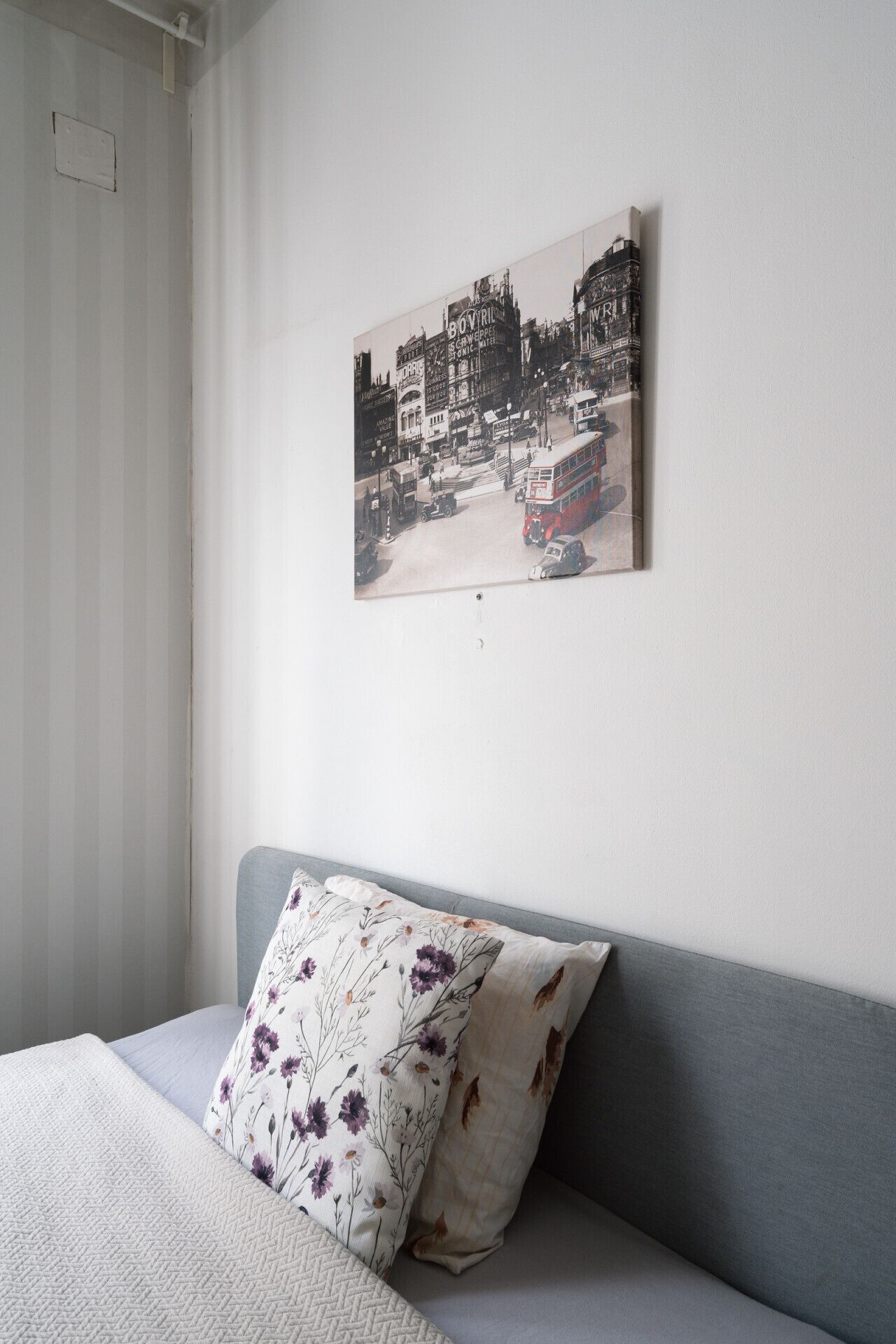 A room with a grey sofa, a floral pillow, and a cityscape artwork on the wall.