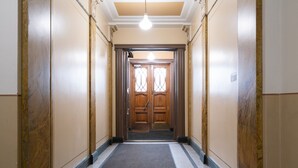 A hallway with a wooden door at the end, a light fixture on the ceiling, and a carpeted floor.