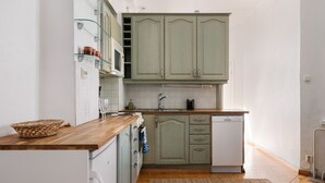 Une cuisine de taille réduite, dotée d’un plan de travail en bois, d’appareils électroménagers blancs et de meubles de couleur vert clair.