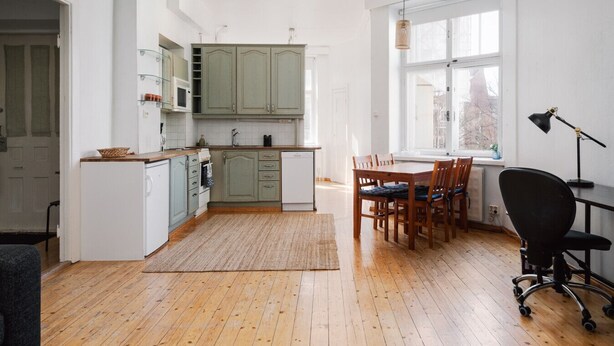 Une cuisine moderne avec un plancher en bois, des armoires vertes et un coin repas comprenant une table et des chaises.