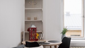 A modern living room with a grey sofa, a dining table with two chairs, a red lantern, and a window with a view of the sky. - Renovated Top Floor Studio in Kallio (Helsinki)