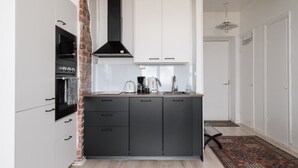 A compact kitchen with a black stove, white cabinets, and a hanging light fixture. - Renovated Top Floor Studio in Kallio (Helsinki)