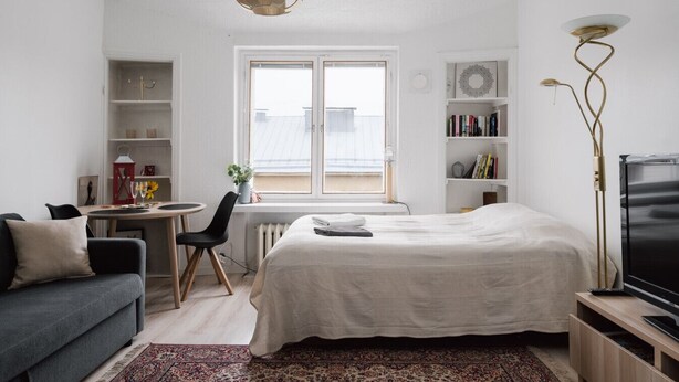 A modern bedroom with a bed, a desk, a chair, a sofa, a TV, and a bookshelf. - Renovated Top Floor Studio in Kallio (Helsinki)
