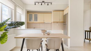 A modern kitchen with light wood cabinets, a central island with chairs, and a large window providing natural light. - Refined 2BR Apartment in Marousi (Marousi)