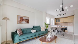 A modern living room with a teal sofa, a wooden coffee table, and a dining area with a kitchen in the background. - Refined 2BR Apartment in Marousi (Marousi)