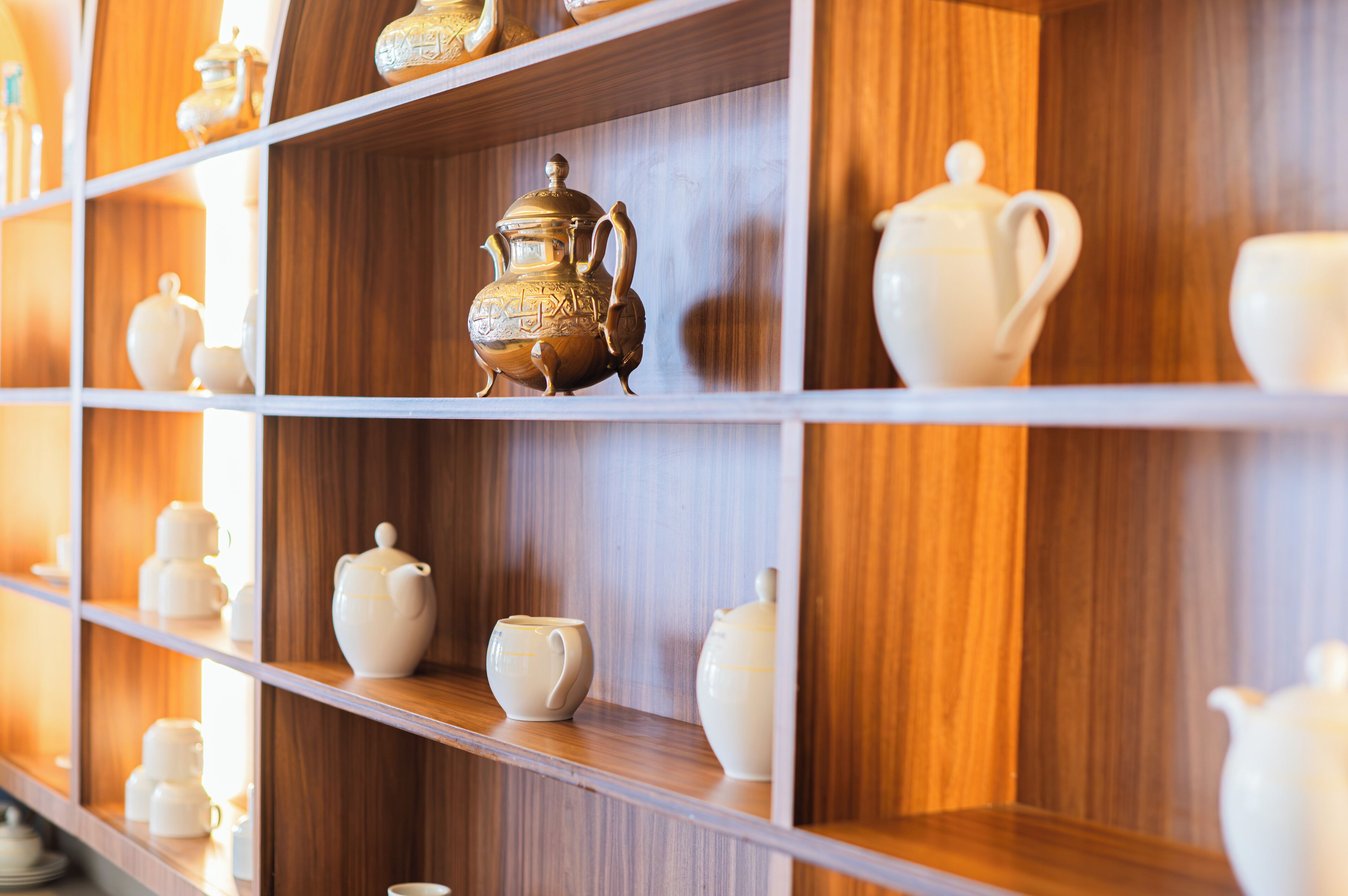 Une étagère sur laquelle sont disposées différentes théières en céramique blanche et une seule théière en laiton décorée.