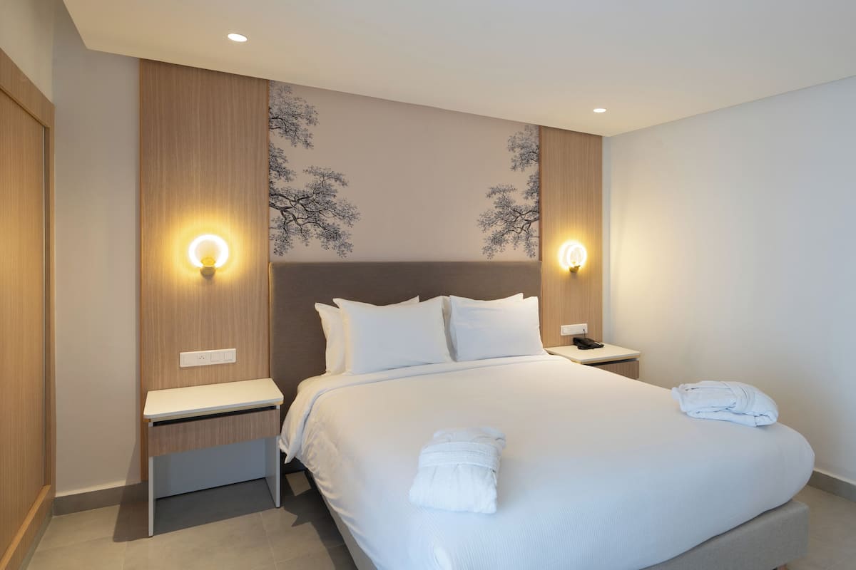 A modern hotel room with a large bed, two bedside tables, a nightstand, and wall-mounted lighting.