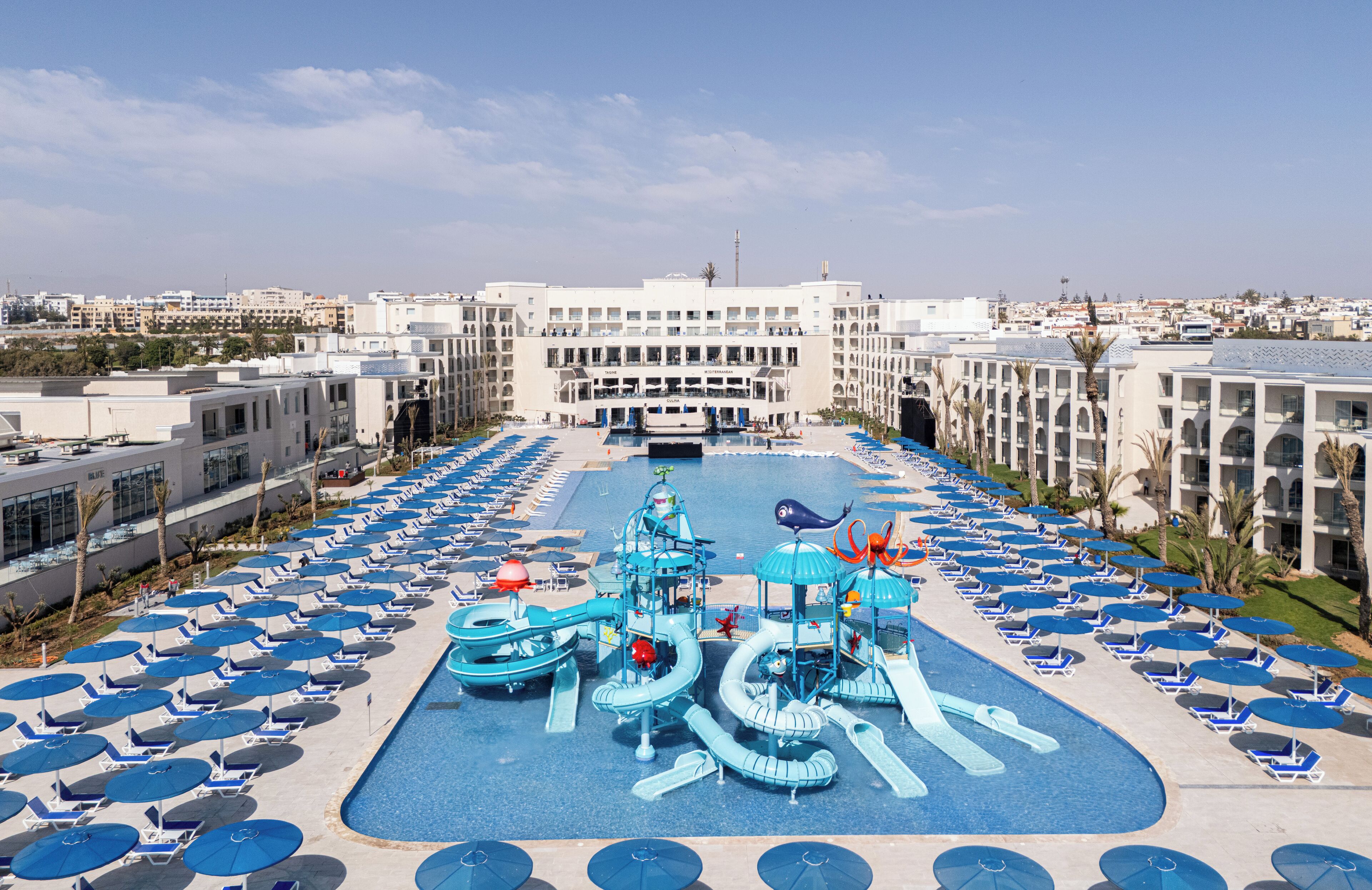 Un espace piscine d’hôtel doté de plusieurs toboggans et de chaises longues.