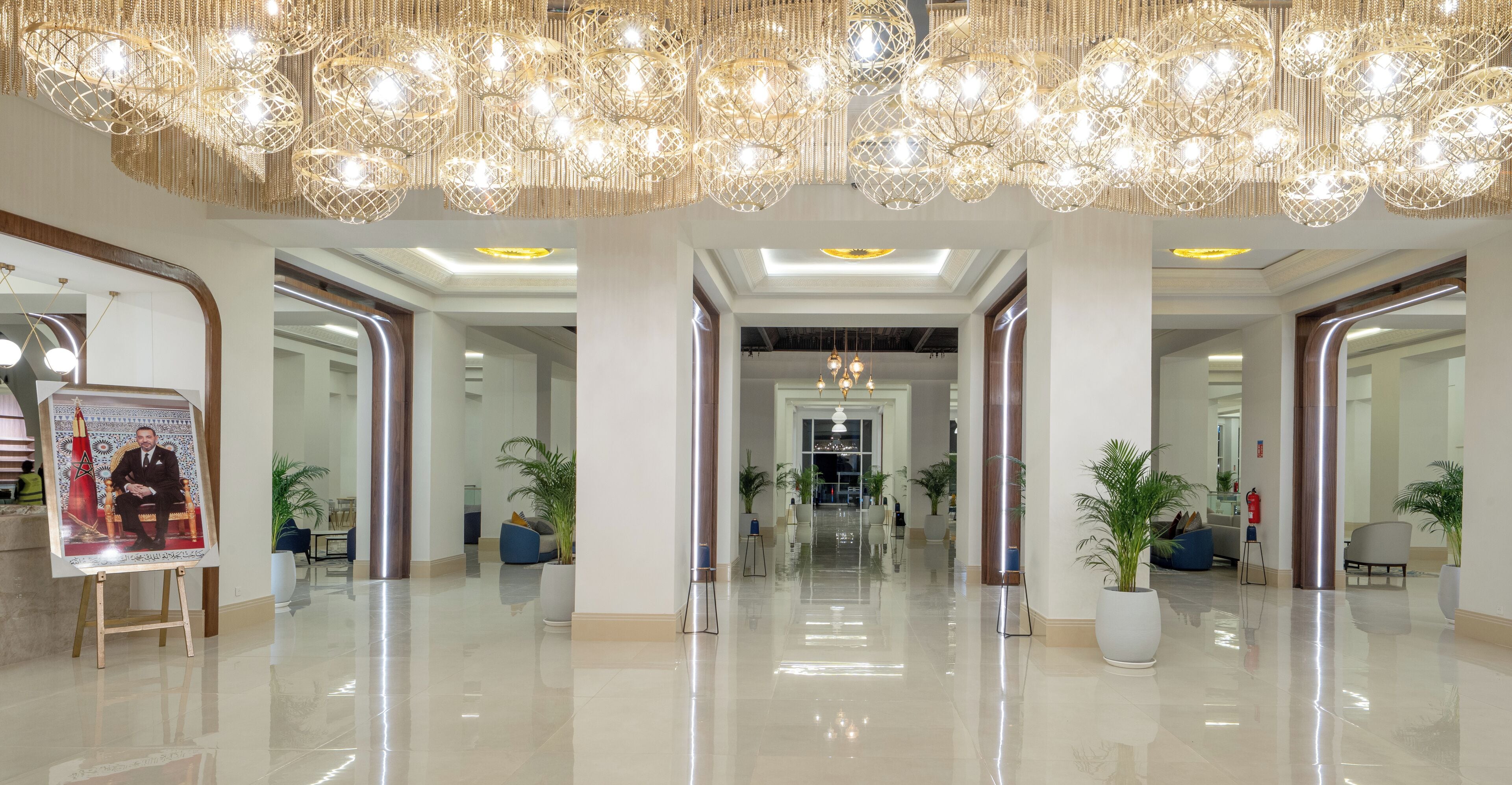 A spacious lobby with a high ceiling, modern chandeliers, and a polished floor.