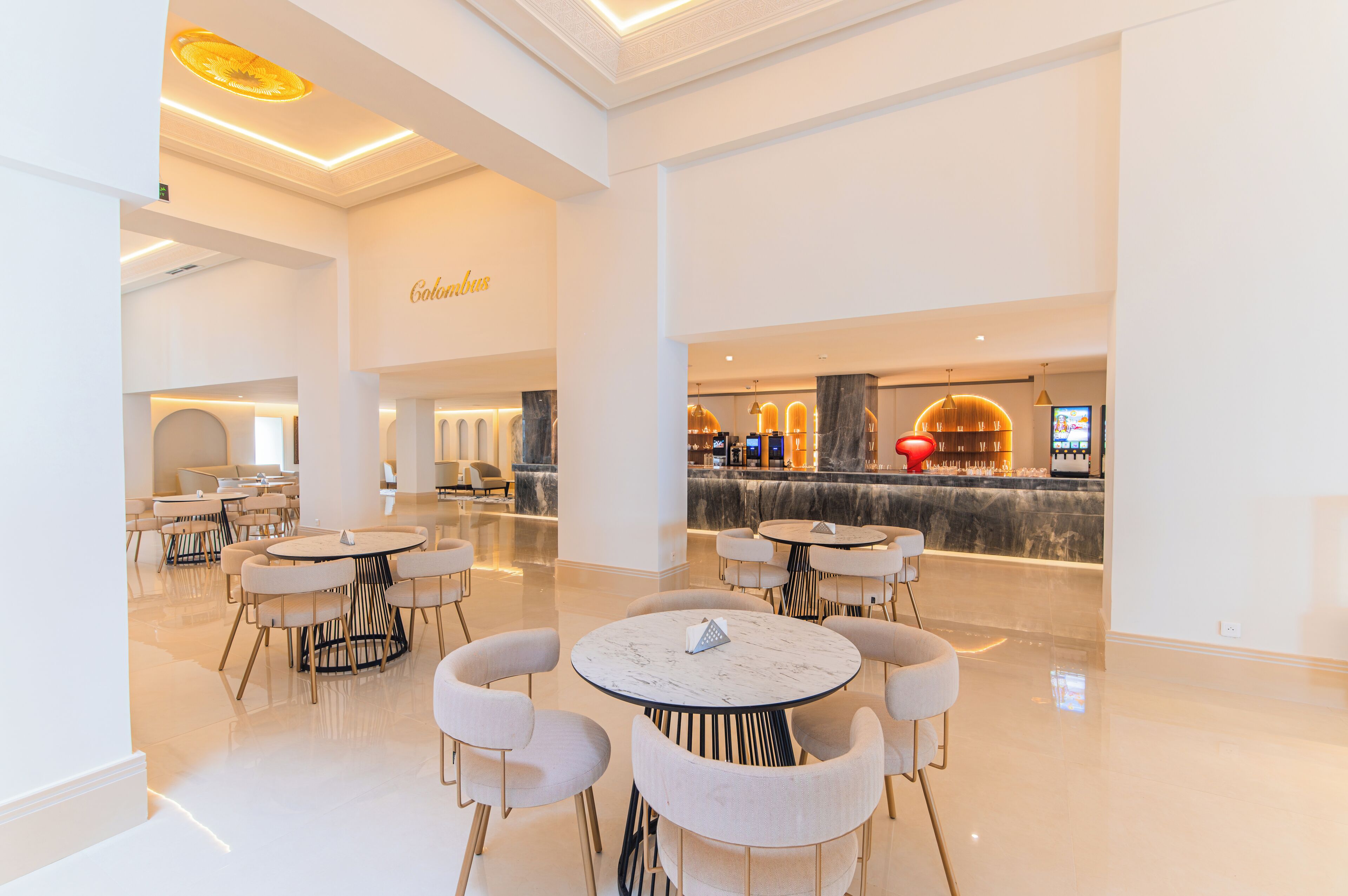 Una moderna hall d'albergo con tavoli e sedie rotonde, un'area bar e una reception.