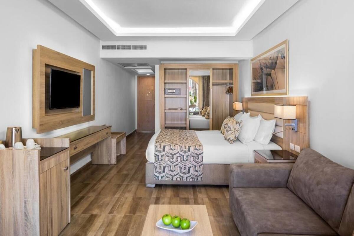 A modern hotel room with a large bed, a sofa, a TV, and a breakfast bar.