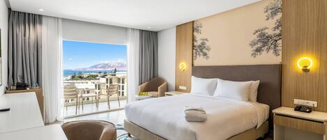 Habitación de hotel con una cama grande, un escritorio, una silla, una mesita de noche y vistas al océano.