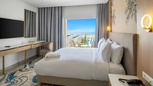 Une chambre d’hôtel avec un grand lit, un bureau, une télévision et une vue sur une piscine et des immeubles.