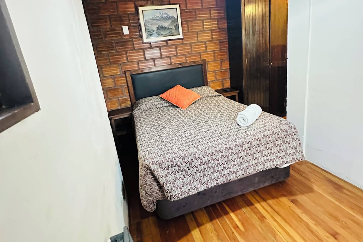 Une chambre avec un plancher en bois, un lit avec une literie à motifs, une tête de lit noire et un tableau au mur.