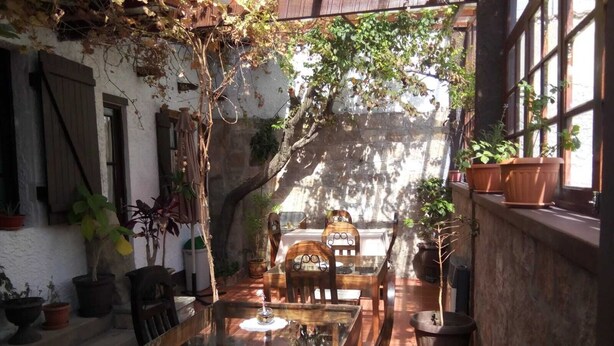 A rustic outdoor dining area with a glass table and wooden chairs, surrounded by potted plants and a stone wall. - Maison de la Bolivie Hotel Boutique (La Paz)