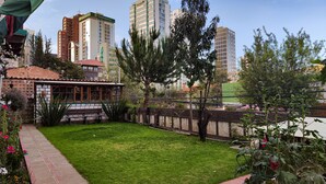 A courtyard with a small building, a grassy area, and tall buildings in the background. - Maison de la Bolivie Hotel Boutique (La Paz)