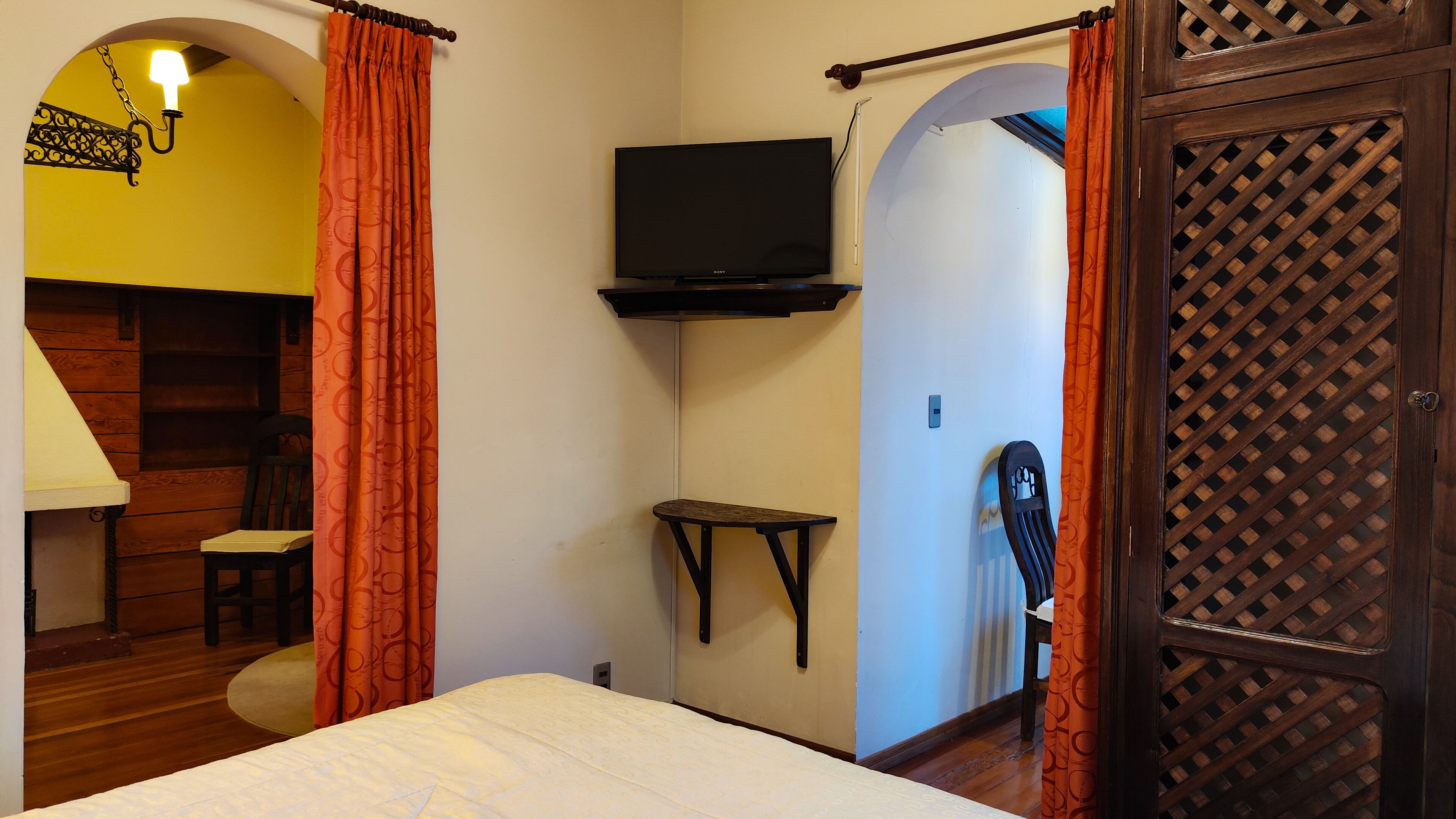 A bedroom with a bed, a TV mounted on the wall, a small table, and a chair.