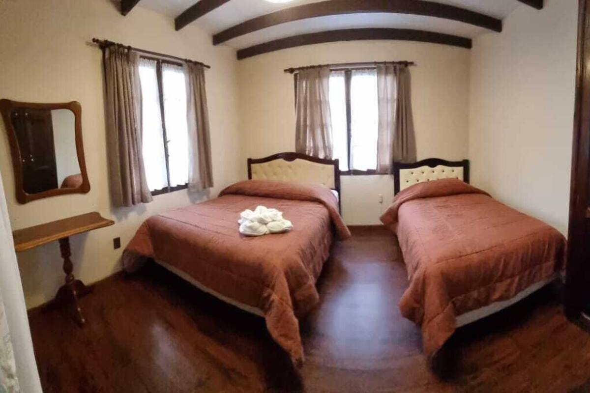 Une chambre avec deux lits, un plancher en bois, un miroir et une porte.