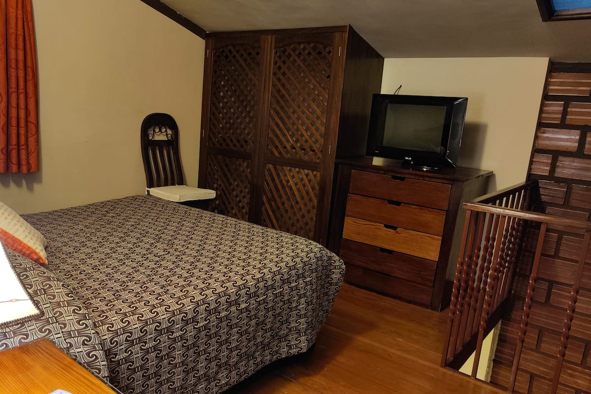 Une chambre à coucher avec un lit, une télévision, une commode et une fenêtre avec des rideaux.