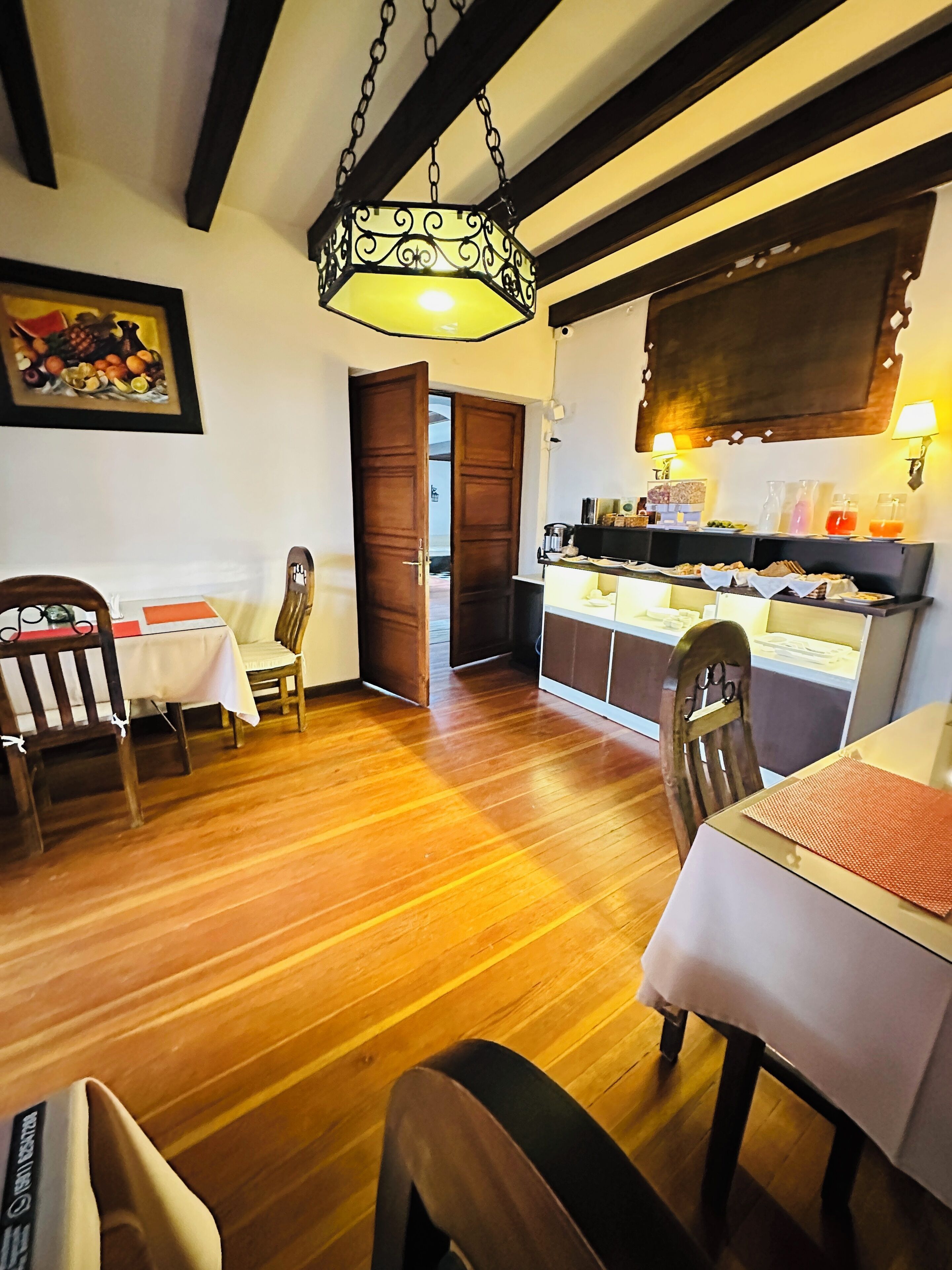 A dining area with wooden flooring, a table with a white tablecloth, and a hanging light fixture.