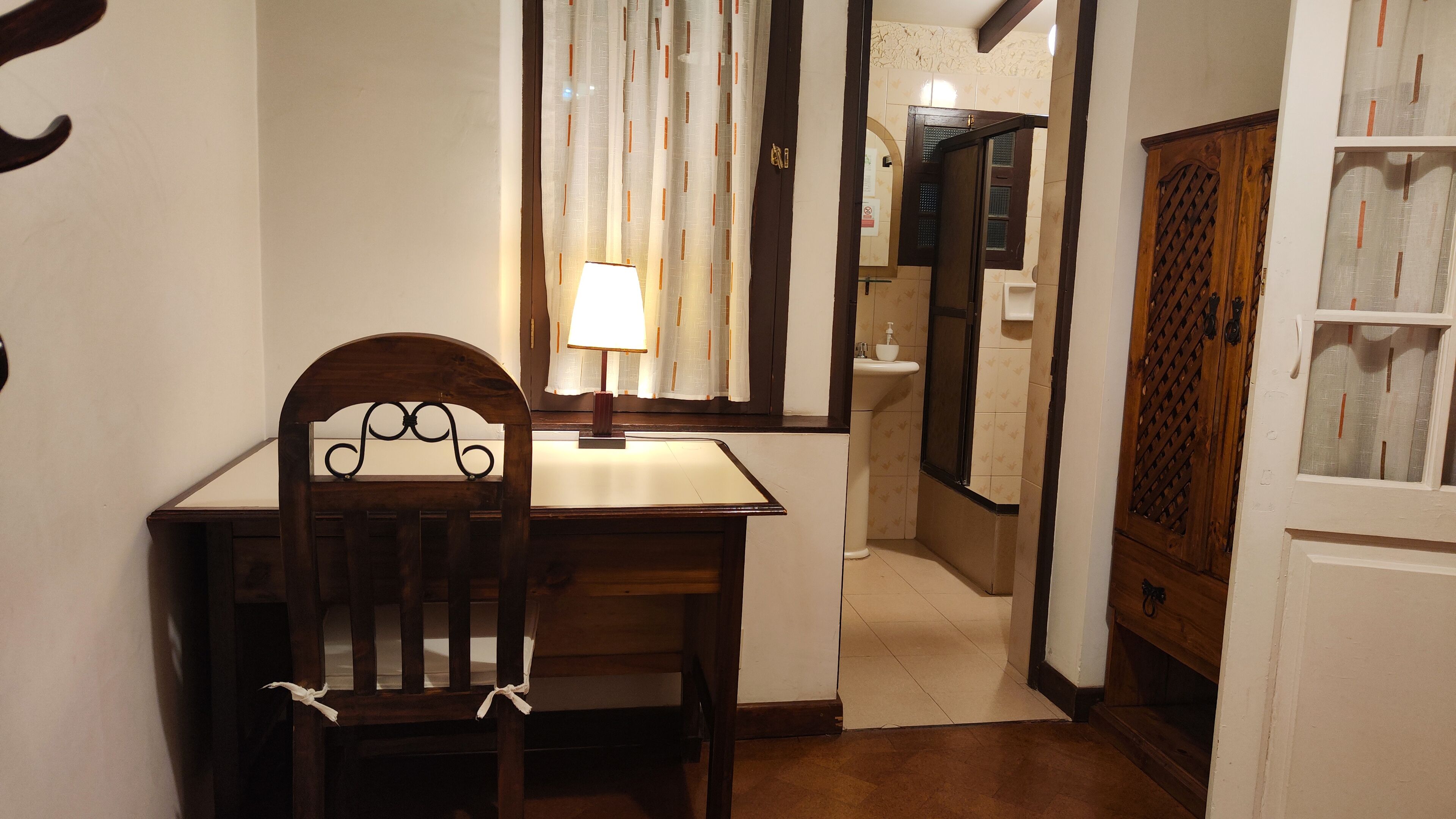 A small, private bathroom with a wooden chair, a desk, and a mirror.