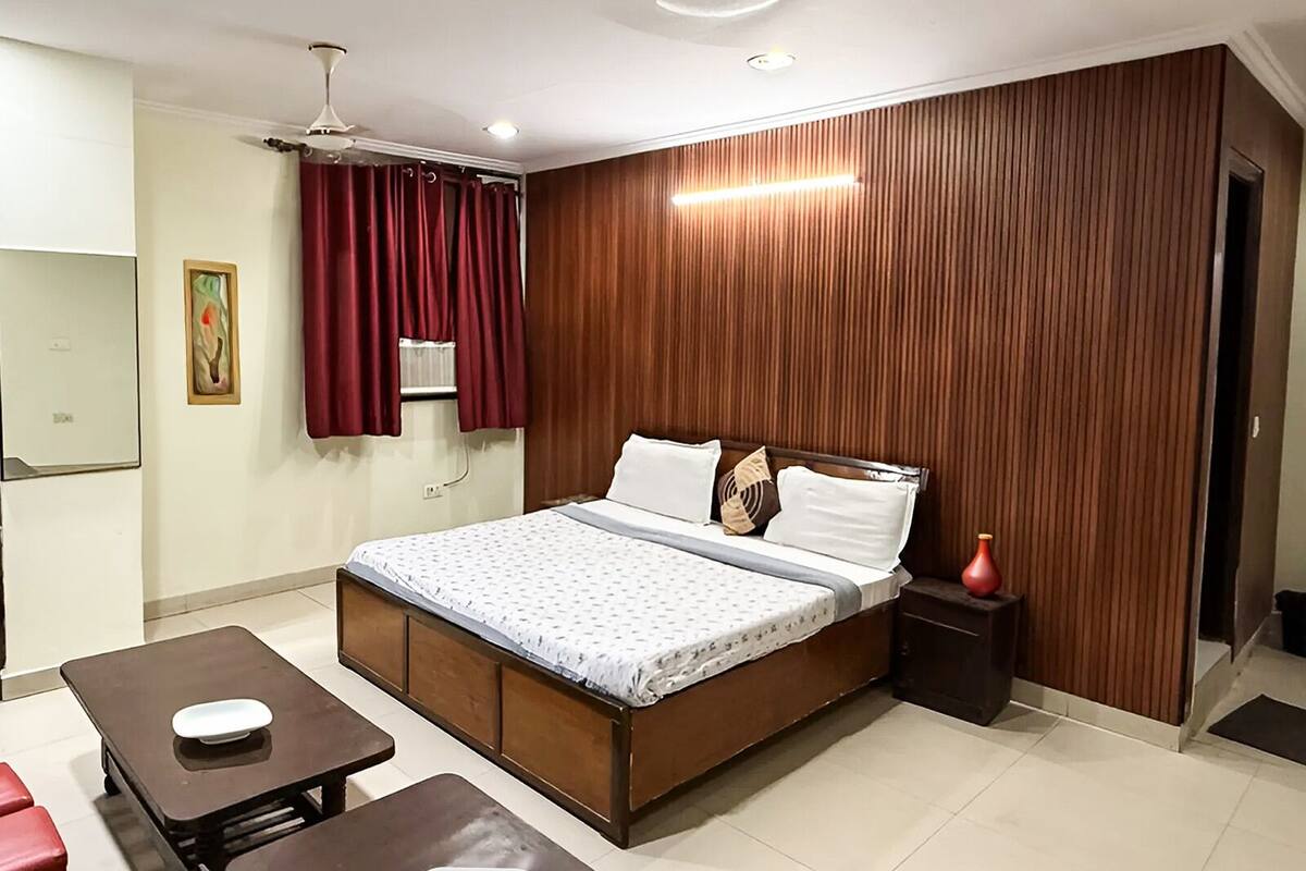 A bedroom with a bed, a bedside table, a small table, and a red chair.
