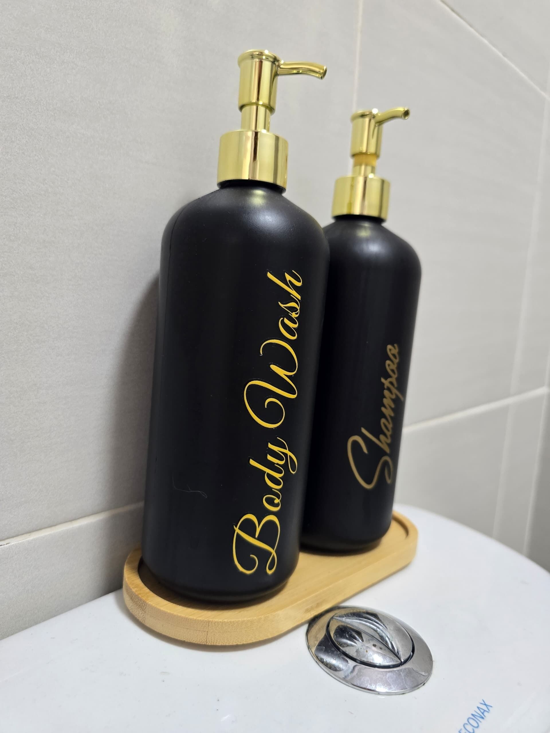 Two black bottles with gold pumps labeled "Body Wash" and "Shampoo" on a wooden tray.